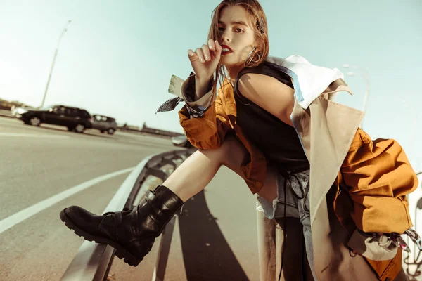 Menina sem emoção atraente em botas de couro pesado encostado em uma cerca de metal — Fotografia de Stock