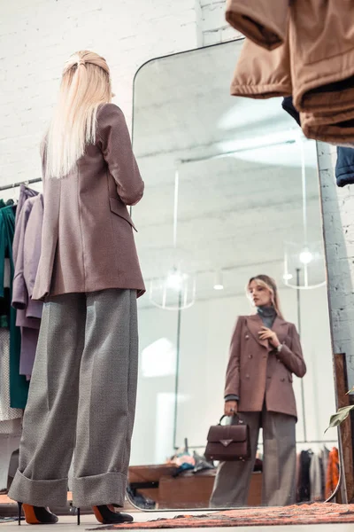 Mujer rubia vistiendo pantalones grises holgados mirando en el espejo — Foto de Stock