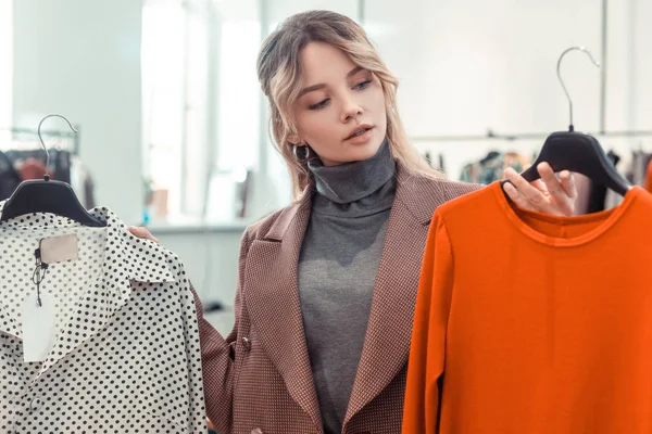 Blonde vrouw kijken naar helder oranje jurk tijdens het winkelen — Stockfoto