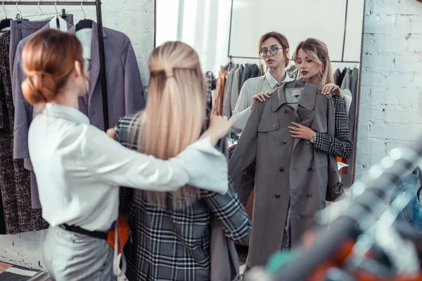 Woman speaking with shopping assistant while choosing coat