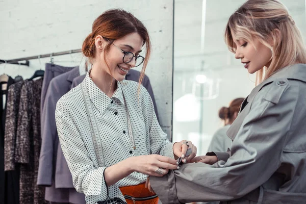 Aangename modeontwerper helpt de klant om trenchcoat te kiezen — Stockfoto