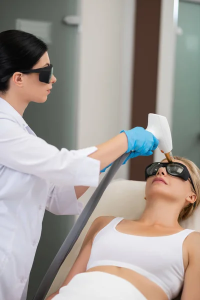 Beauty doctor with laser standing above her patient.