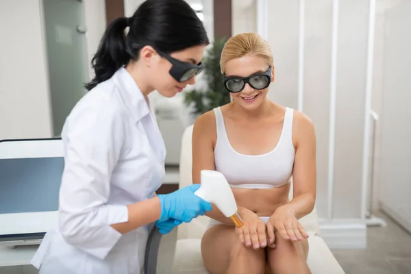 Mujer mirando cómo cosmetólogo haciendo sus procedimientos láser . — Foto de Stock