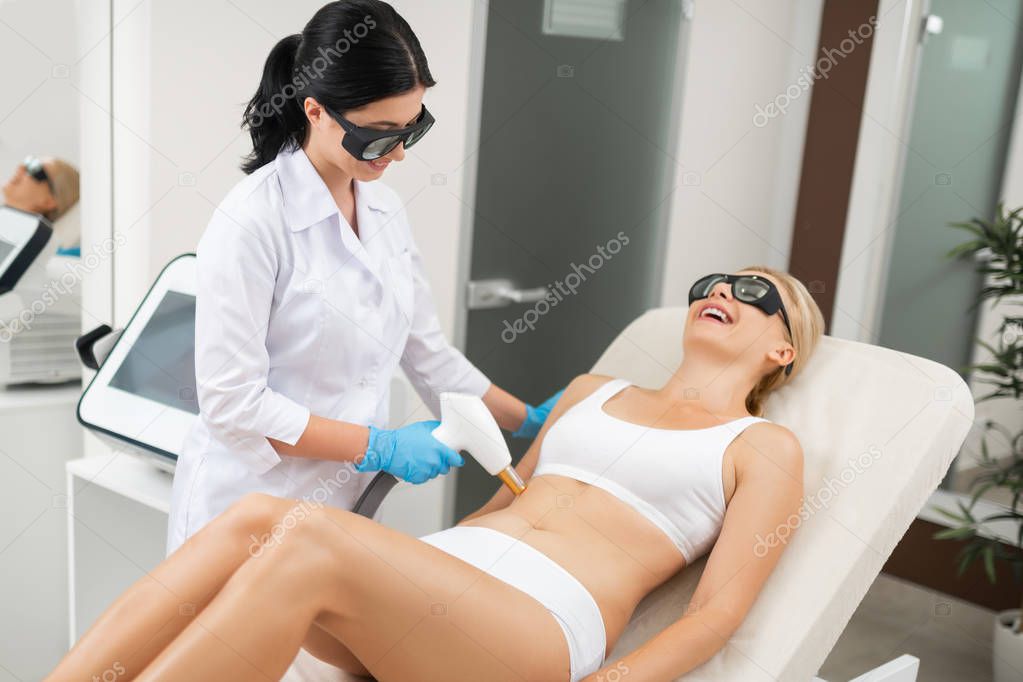 Woman laughing during laser procedures in a beauty salon.