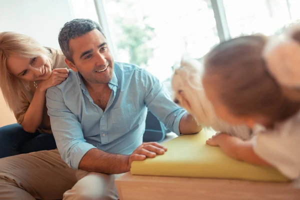 I genitori guardando la loro figlia che gioca con il cane bianco soffice — Foto Stock