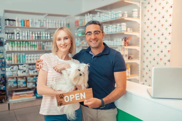 Empreendedores segurando cão branco depois de abrir própria loja de animais — Fotografia de Stock