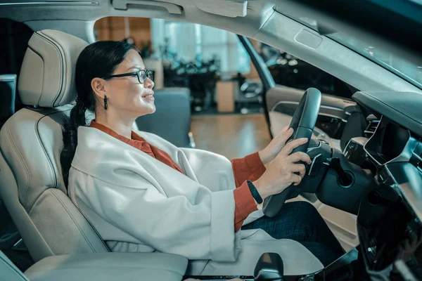 Mujer sentada al volante en la sala de exposición de automóviles . —  Fotos de Stock