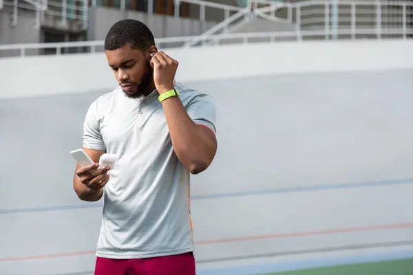 Serious man putting wireless earphones in his ears