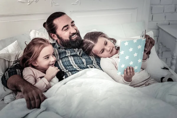 Papá acostado en la cama con sus hijos leyendo la historia para ellos —  Fotos de Stock