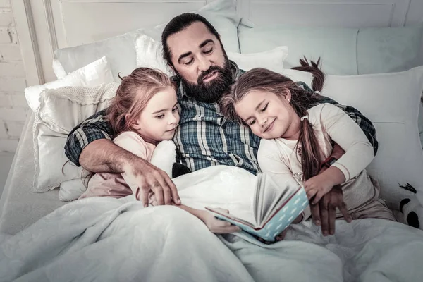 Dad and daughters cuddling in bed reading book
