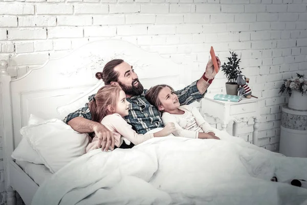 Papá sonriente y dos niños tomando selfies en la cama —  Fotos de Stock