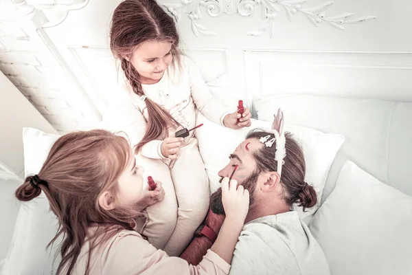 Szczęśliwy uśmiechnięty dziewcząt malarstwo na tatusiowie twarz podczas on drzemki — Zdjęcie stockowe