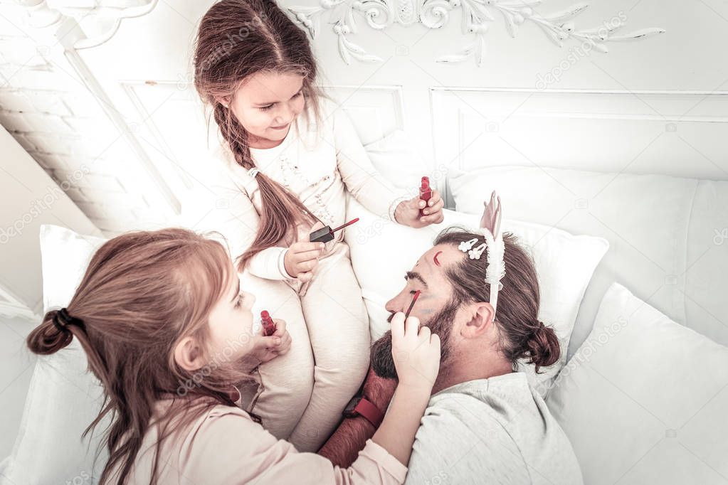 Happy smiling girls painting on dads face while he naps
