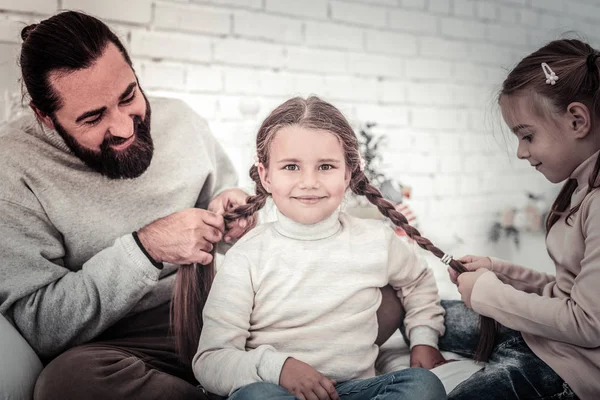 Pequeña linda chica teniendo su pelo trenzado por la hermana y el padre —  Fotos de Stock