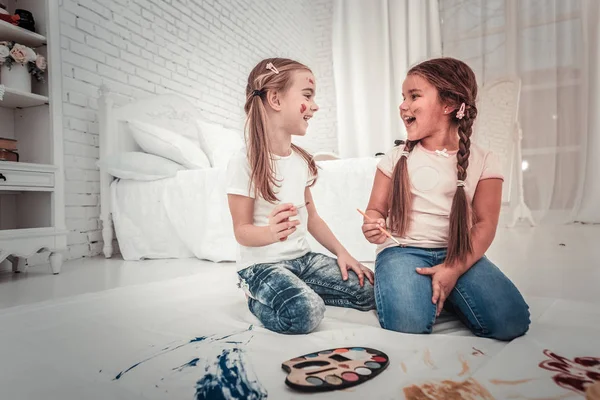 Två söta tjejer i vit tshirt och jeans målning sitter på sovrummet golvet — Stockfoto