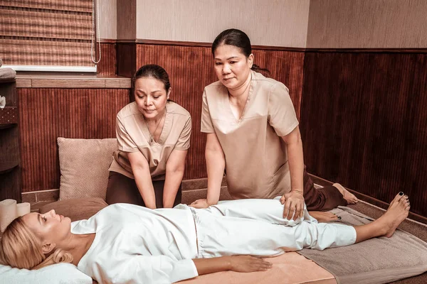 Dois massagistas concentrados trabalhando com seu cliente . — Fotografia de Stock