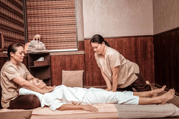 Duas massagistas ajudando seu cliente a relaxar . — Fotografia de Stock