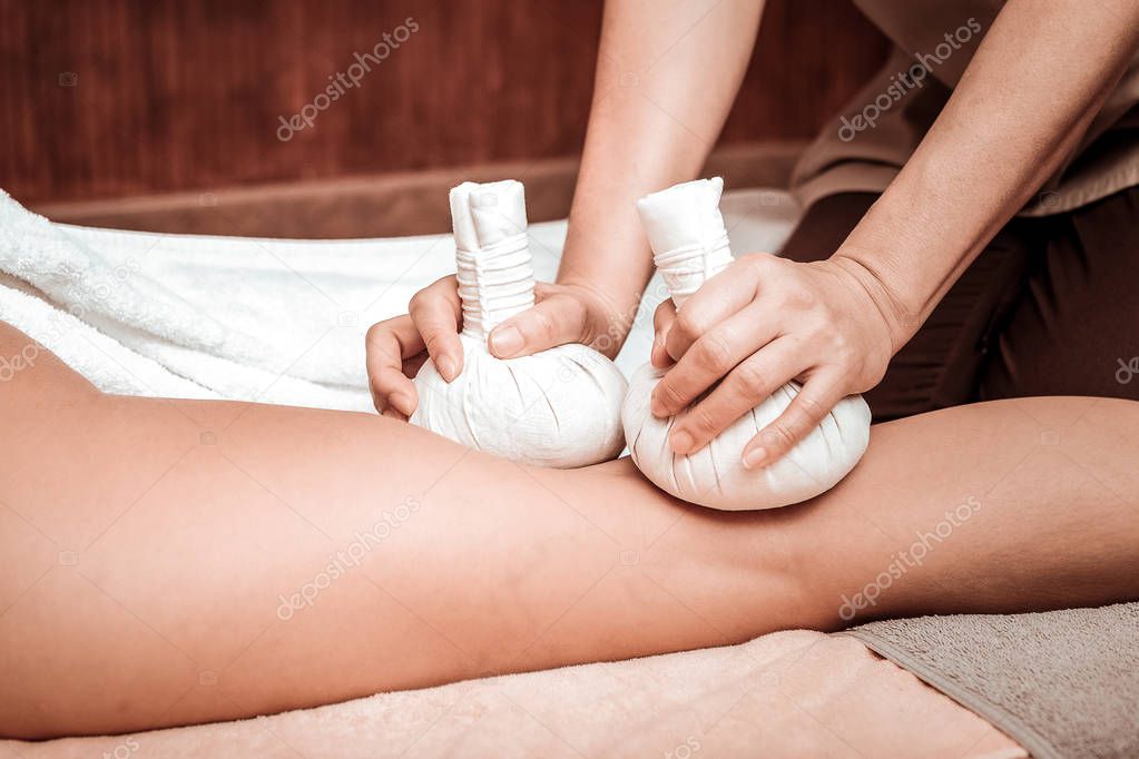 Herbal bag massage of legs in massage salon.