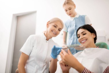 Dentist helping her patient choosing teeth whitening samples. clipart