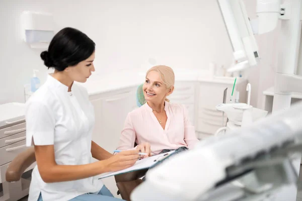 Glad patient frågar sin tandläkare om förfaranden. — Stockfoto