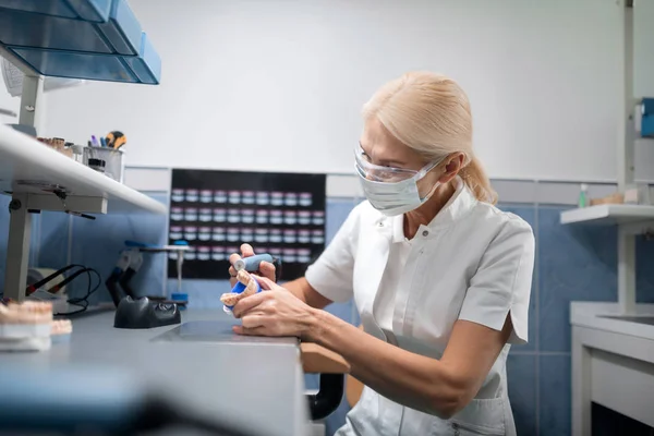 Technik dentystyczny polerowanie protezy dentystycznej w jej biurze. — Zdjęcie stockowe