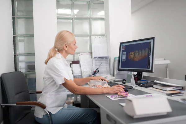 Dental technician examining model of teeth on computer.