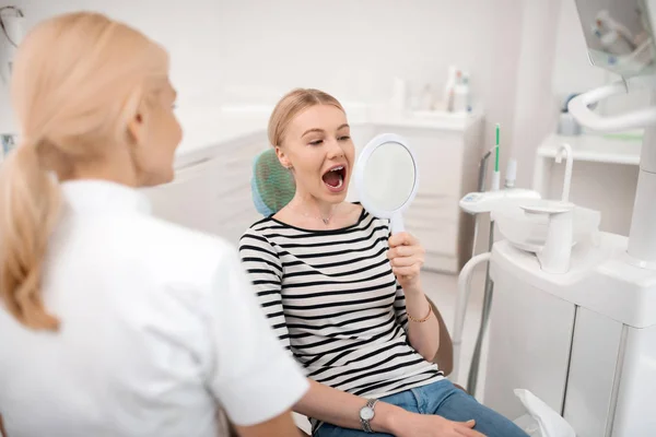 Dentistas paciente olhando para os dentes no espelho . — Fotografia de Stock