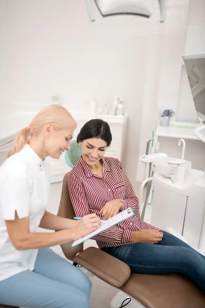 Vrouw helpt haar tandarts vullen van medische aanvraagformulier. — Stockfoto
