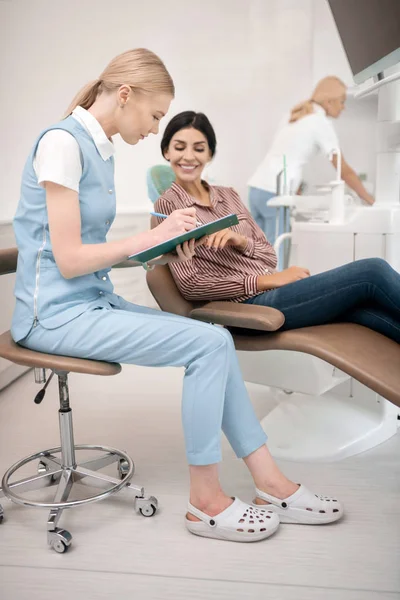 Pacjent dentysta wypełniając formularz z asystentem. — Zdjęcie stockowe