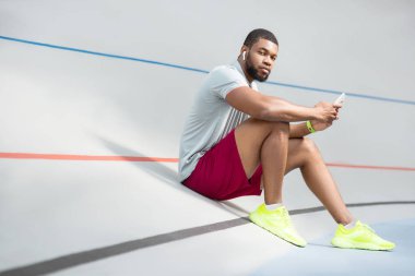 Rahat genç sporcu bir akıllı telefon ile açık havada oturan