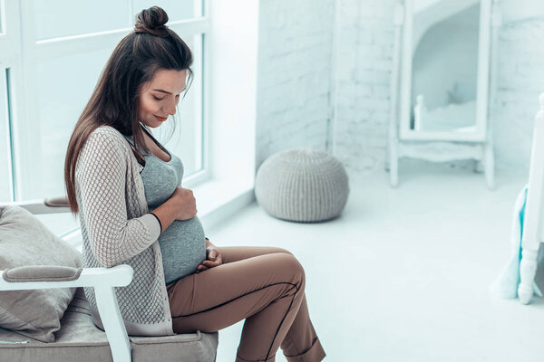 Tender brunette girl looking at her big belly