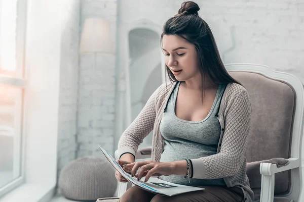 Koncentrerad gravid kvinna läser tidningen hemma — Stockfoto