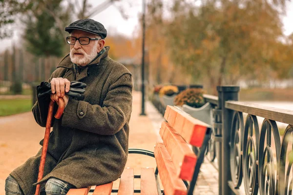 Uomo anziano seduto nel parco appoggiato sulla canna — Foto Stock