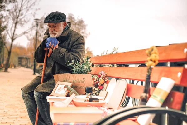 Vista laterale di un povero uomo triste seduto sulla panchina a vendere roba — Foto Stock