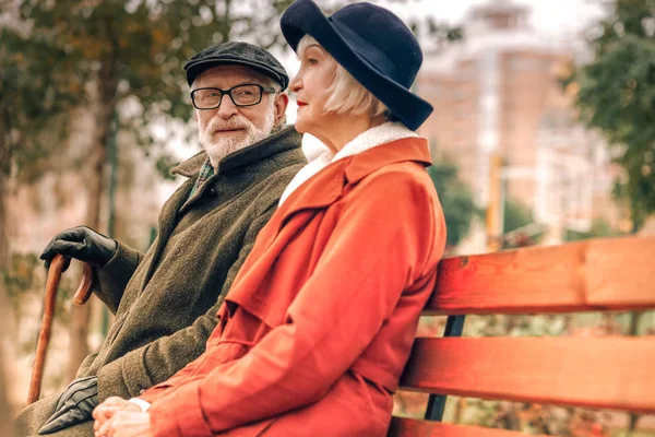 Старший мужчина любовно смотрит на свою жену, сидящую на скамейке в парке — стоковое фото