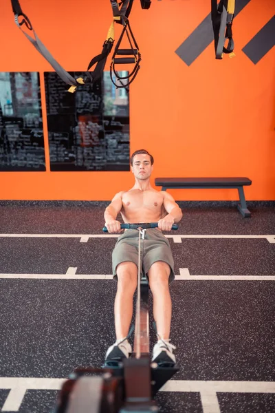 Bonito homem ajuste de formação em uma máquina de exercício desportivo — Fotografia de Stock