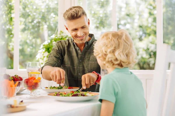Bello marito sorridente mentre taglia l'insalata per suo figlio riccio — Foto Stock