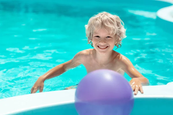 Lindo chico rubio rizado sonriendo mientras nada en la piscina — Foto de Stock