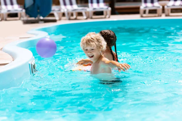 Hermano riendo mientras jugando pelota con hermana en piscina — Foto de Stock