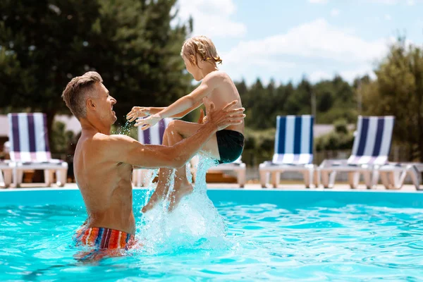 Papa gooit zijn zoon in water terwijl je plezier hebt in het zwembad — Stockfoto
