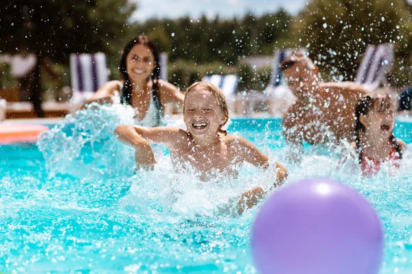 A szülők és a gyermekek nevetve, miközben játszik a labdát a medencében — Stock Fotó