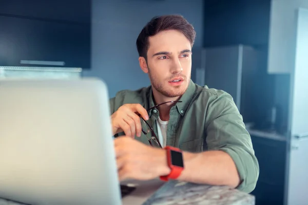 Jovem sério sentado perto do laptop em casa — Fotografia de Stock