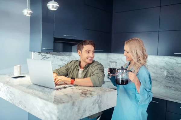 Vriendin brengt koffie voor haar man werken op laptop — Stockfoto