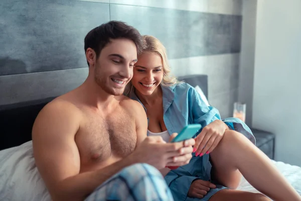 Casal assistindo fotos no smartphone deitado na cama — Fotografia de Stock
