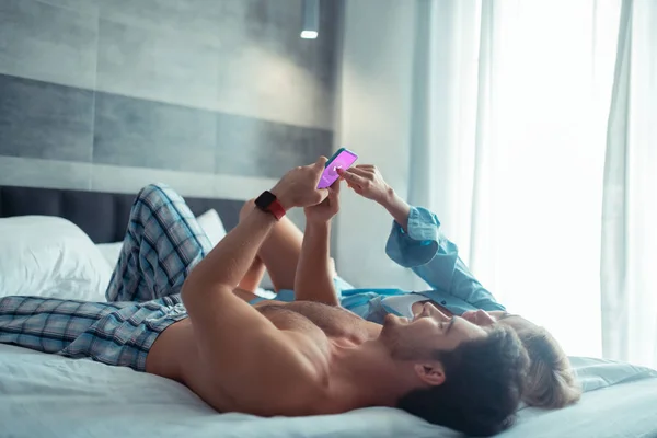 Couple chilling on bed and using smartphone together — Stock Photo, Image