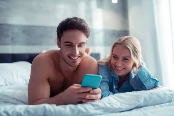 Casal rindo enquanto assiste vídeo engraçado refrigeração na cama — Fotografia de Stock