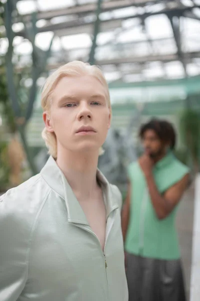 Blonde-haired male model posing in greenhouse with colleague