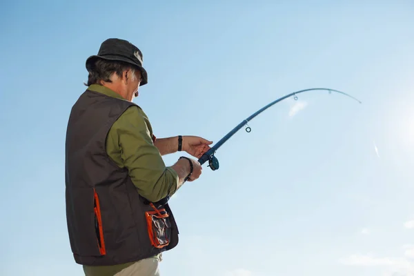 Retired man pulling fishing tackle after catching fish — Stock Photo, Image