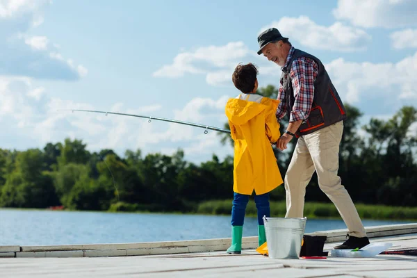 Smiling grandfather giving fishing tackle to grandson — Stock Photo, Image