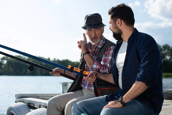 Bearded grey-haired man teaching son catching fish — Stock Photo, Image